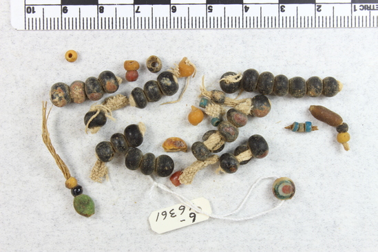 Hearst Museum object titled Beads, accession number 6-16361, described as Beads: a) spherical beads on 16 fragments of original string b) cloth fragments