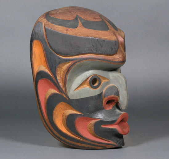 Hearst Museum object 3 of 3 titled Mask, accession number 2-66925, described as Wood, red cedar, anthropomorphic, polychrome in natural, red, grey and brown. Beaked nose, prominent nostrils, lips pursed for whistling/singing, eyes (black rimmed circular holes) under heavy black eyebrows. Equipped with 2 small eyebolts and wire. Back inscribed, "Chiefs Mask" "Jack James, Gilford Isle, B.C." Commercial paint.