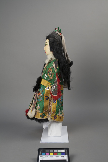 Hearst Museum object 3 of 6 titled Hand puppet, accession number 9-22420, described as Puppet, hand:  Princess.  A.  Head:  carved wood, white with red, green, black and brown features, long black hair, 3 sections tied with red fabric, bun tied with gray and green fabric and wire.  B.  Body:  white cloth.  Legs:  brown checked cloth.  Hands:  white wood.  Boots:  black and white boots.  C. Robe:  cloth, green with yellow, blue and orange appliques, multi-colored sequins and mirrors, red, white and black rabbit fur trim.  47 x 29 cm (18 1/2 x 11 7/16 in)