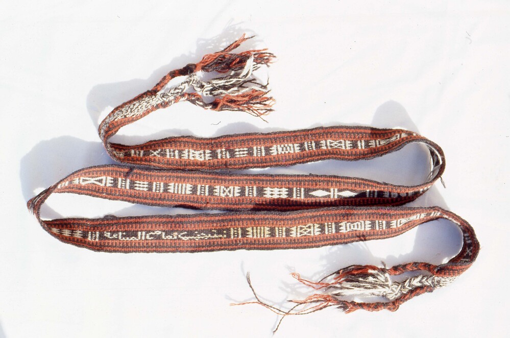 Hearst Museum object titled Color slide, accession number 25-25275, described as 35mm color slide transparency. Woven rope-like object with striped and triangle patterns; featuring fringed detailing; colored red, black, and white.