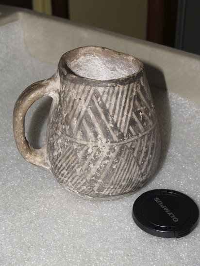 Hearst Museum object 3 of 3 titled Mug, accession number 2-65925, described as Mug with single handle; buff pottery; 2 bands of zigzags with diagonal fillers around the exterior.  The rim is chipped.  Pueblo III per Larry Dawson.