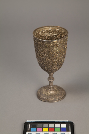 Hearst Museum object titled Tin goblet, accession number 9-11928, described as Wine goblet: chased silver; rims at top and base have knobby rings; otherwise, entire surface covered with floral-leafy arabesques; stem has leaves divided by round protuberance; length 19.7 cm; width 9.6 cm