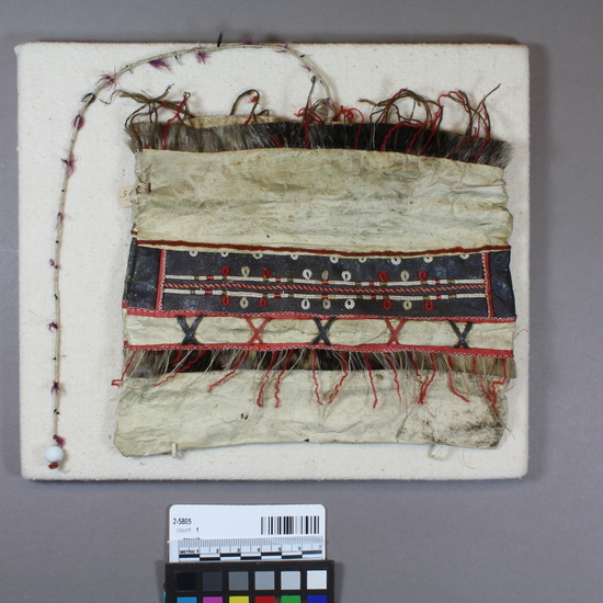 Hearst Museum object 2 of 2 titled Pouch, accession number 2-5805, described as Scraped stomach or intestines, tanned white. Made in 7 horizontal panels, largest one folded over for a seamless bottom. No decoration in side seams. Main decoration is horizontal fringing of seal hair, red yarn, white reindeer hair embroidery and red-painted depilated hide or gut, about 5 cm from bottom. Next, a wide black graphite-painted horizontal panel with white reindeer hair embroidery and loop-fringing, red and gray yarns and threads, and red-painted gut strips. White windpipe skin inset with black & red dyed gutskin and seal fur; trimmed with white quill and red wool yarn. Bag string: braided white cotton yarn into which pink, black tufts of cotton have been mixed, at end a white glass bead.
