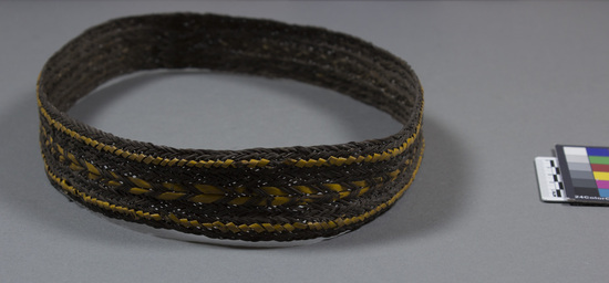 Hearst Museum object titled Belt, accession number 11-40180, described as Fern stem man's belt with orchid-stem decoration. Belt, dark-brown fiber braided in herringbone pattern; decorated with two border rows of wrapped orchid stem and central herringbone threading of orchid stem. Diameter 22.8 cm., height 3.5 cm.