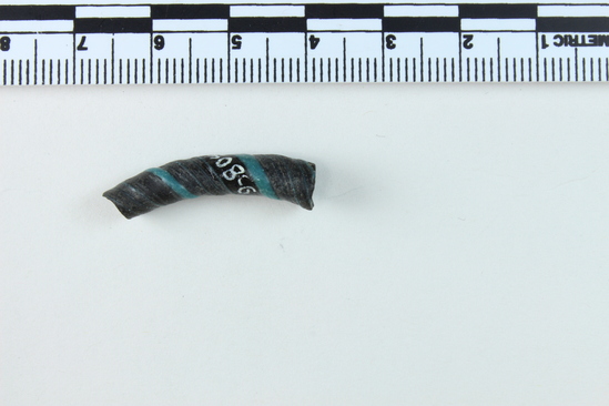 Hearst Museum object 5 of 6 titled Bracelet fragment, accession number 9-8049, described as Glass bracelet frag.; opaque black, twisted, curved rod w/ blue spiral; 27 x 7 mm.