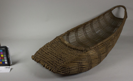 Hearst Museum object 2 of 3 titled Cradle, accession number 1-164484, described as Twined basketry.  Tag "Klamath R. Tribes Att.". Per Ralph Shanks:  Twined openwork baby basket.  The warp material is probably willow, possibly hazel.  The wefts are of uncertain material.  At the foot there is plain twining, spaced closer than the rest of the basket.  The rim is covered,  reinforced with rods.  Starting at the foot there are sets of three paired weft rows all the way to the handle.  The basket has alternating slants of weft twists, often switching by weft row.  The basket is from Northwestern California.