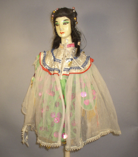 Hearst Museum object 6 of 6 titled Hand puppet, accession number 9-22235, described as Puppet, hand.  Foreign Princess A.  Head: carved wood, light orange with pink, green and black features, long, black hair with beads in it  B. Body: red and pink flowered print cloth,  Boots:  wood, black and white.  C. Dress: green cloth with purple sequins, sheer white overlay  48 x 31 cm (18 7/8 x 12 3/16 in)