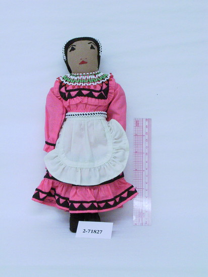 Hearst Museum object titled Female doll, accession number 2-71827, described as Stuffed cloth doll.  Choctaw, cotton embroidery features, embroidery floss hair.  Rose colored cotton dress decorated w/ black applique bands.  Green, red & white beaded collar.  White & black beaded head band & belt, white fabric apron and petticoat.  Black fabric boots.