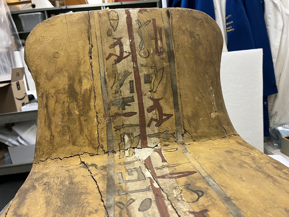 Hearst Museum object 124 of 167 titled Coffin, accession number 6-19912, described as Wooden anthropoid coffin. Inscription running down center of lid. Determined by Kea Johnston to probably be the outer coffin of Iwefaa (6-19928, 12-11039). According to Kea Johnston, "This coffin belonged to a man named Iwefaa, whose name is inserted in the middle of the spells written in the two columns on the front. This coffin is likely the outer coffin for PAHMA 6-19928 based on the similarity of the owner's name, unusual costume, and the paleography of the inscription. Both coffins were purchased on the antiquities market by George Reisner for Phoebe A Hearst. However, stylistically, they are very similar to a set of coffins known to have come from the site of Akhmim, which was excavated in the 1880s by Gaston Maspero, and which has heavily looted for the antiquities market during this decade." "The pectoral vignette between the text and the collar shows the deceased standing before squatting baboon and is the source of our logo. The hieroglyph for 'sky' is above their heads, and the side borders are formed by a pyramid and the symbol for the West.