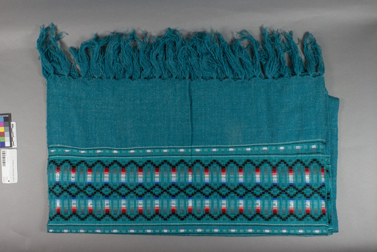 Hearst Museum object titled Shawl, accession number 16-20224, described as Shawl; 62 x 180 centimeters, plus 12 centimeter fringe; turquoise yarn with a clear synthetic fiber spun into yarn; woven color bands 15 centimeter from each end; colors:  white, grey, black, red and blue in the bands.