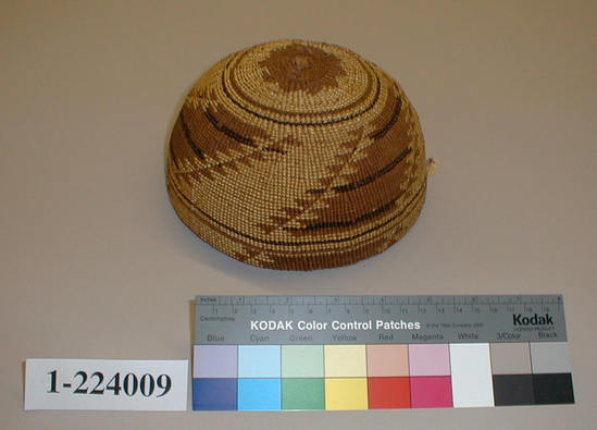 Hearst Museum object titled Cap, accession number 1-224009, described as Basketry hat, twined.  Tag "Very fine old Indian basket N W $25_00". Per Ralph Shanks:  Twined woman's basket hat. Crossed warp starting knot.  The warp material is probably willow or hazel. The weft material is conifer root.  The weft overlay design is beargrass and maidenhair fern. Starting at the starting knot, there are two weft rows of plain twining, followed by three strand twining for 1/4 inch, followed by 1 inch of plain twining, followed by one weft row of three strand twining.  Plain twining continues to the rim where there is one weft row of three strand twining 1/2 inch below the rim.  The rim is trimmed.  The main design is three sets of beargrass diagonals outlined in triangles. The basket has a rightward work direction, with an up to the right slant of weft twist.  The workface is on the exterior.  The overlay is single-sided, with the design on the exterior.  The basket is from Northwest California.  There are some gray, possibly animal, hairs on the interior.