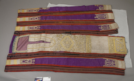 Hearst Museum object titled Robe, accession number 5-7901, described as Robe, strips of purple between bands of red ribbon; main front panel solid gold braid and sequins; solid on purple stripes across shoulders and around hem; armholes outlined in gold braid; square neck deeply slit down front; length: 122 cm. Silk with braid, gold braid and sequins. Made by sewing strips of material together lengthwise, leaving slits for sleeves. Silk in fragile condition.  material woven at Kurdassah village, Egypt- attribution fide Susan (Mrs. Kent) Weeks, Jan. 1980