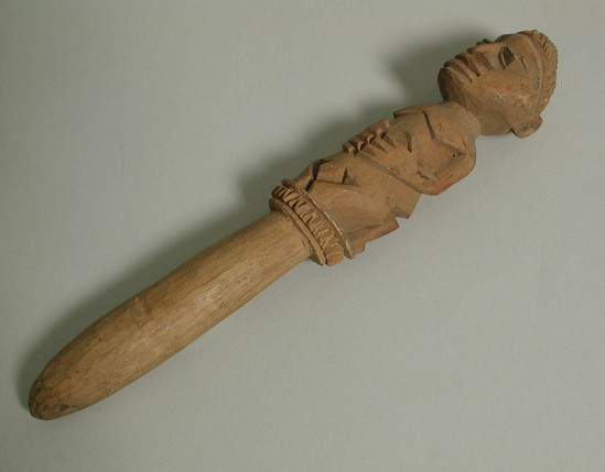 Hearst Museum object titled Bell, accession number 5-11714, described as Ifa 'bell';  carved wood, light in color, shaped like a staff, top portion consists of a kneeling male figure;  23 cm long, 3.5 cm wide.