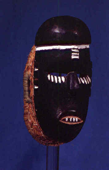 Hearst Museum object titled Mask, accession number 5-1949, described as Ceremonial head mask, carved wooden face with incised designs in white. Painted black. Basketry backing. Length 25.5 cm. Wide 14 cm. Made by local carver; Chukwu Okoro.