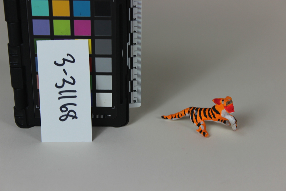 Hearst Museum object titled Figure, accession number 3-31168, described as MINIATURE ANIMAL FIGURE:  Ceramic tiger figure.  Animal is running so legs are widely splayed.  Belly and inside legs is white; upper body, head and legs are day-glow orange w/ black stripes.  Mouth is red.  (NOTE: One leg is missing, plus the upper part of his snout) H=2.8cm W=2.7cm L=6.1 cm
