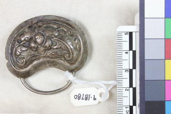 Hearst Museum object titled Netsuke, accession number 9-18780, described as Netsuke; rattle/bell, kidney shaped, with plain wire handle attached at top; scroll and leaf design on one side, symbols, leaf and scroll design on other; H 4.7 cm X W 4.8 cm