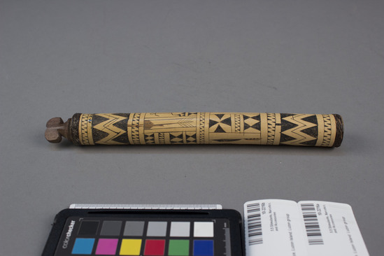 Hearst Museum object 2 of 3 titled Lime container and stopper, accession number 10-2216a,b, described as A) Bamboo lime container, decorated with incised geometric designs and stick figures; band of plaited rattan around one end; 8¾ inches long; B) wood stopper in shape of Bontre headdress.