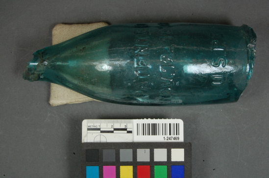 Hearst Museum object titled Glass bottle fragment with maker's mark stamp, accession number 1-247469, described as Glass bottle; neck; body; blue embossed lettering