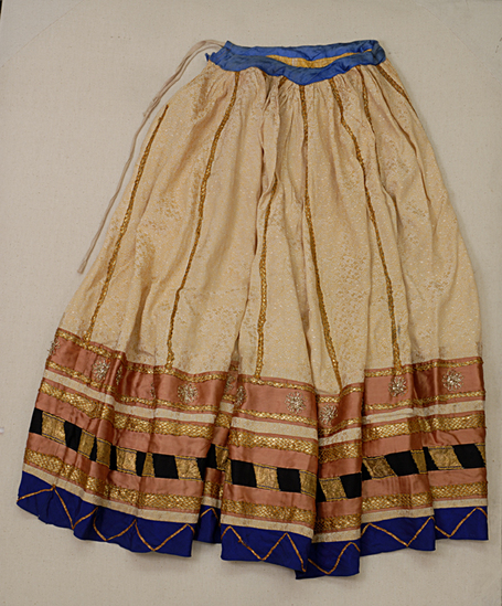 Hearst Museum object titled Skirt, accession number 9-11228, described as skirt; yellow satin brocade with bands of red satin blue taffeta and black cotton around the hem; gold coloured braid and tinsel trim; gathered onto a blue satin band with a drawstring closure; Lemgth 94 cm.