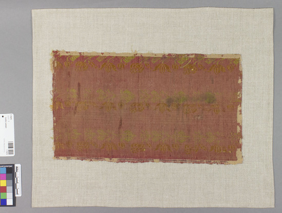 Hearst Museum object titled Textile sample, accession number 7-7679, described as Silk framed piece with red ground, green, and orange designs, and floral designs in stripes; plain weave, brocaded; 12 3/4 by 1 1/8".