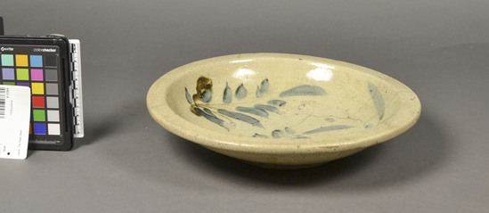 Hearst Museum object titled Plate, accession number 9-12264, described as Plate, ceramic, wide bowl shape with flanged rim, brush stroked wisteria blossom decoration in blue and brown underglaze on center top, with a creamy white translucent overglaze, only the short foot is not glazed, many chip marks left from firing, broken and mended. Maximum diameter 29 cm, height 6 cm.