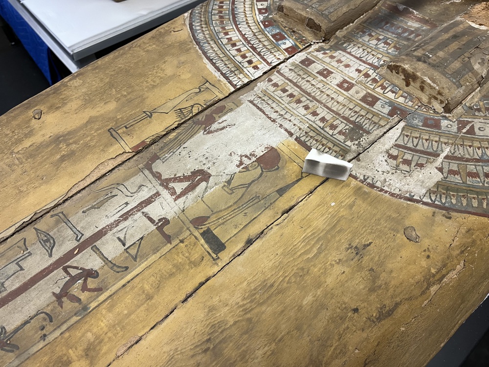 Hearst Museum object 11 of 167 titled Coffin, accession number 6-19912, described as Wooden anthropoid coffin. Inscription running down center of lid. Determined by Kea Johnston to probably be the outer coffin of Iwefaa (6-19928, 12-11039). According to Kea Johnston, "This coffin belonged to a man named Iwefaa, whose name is inserted in the middle of the spells written in the two columns on the front. This coffin is likely the outer coffin for PAHMA 6-19928 based on the similarity of the owner's name, unusual costume, and the paleography of the inscription. Both coffins were purchased on the antiquities market by George Reisner for Phoebe A Hearst. However, stylistically, they are very similar to a set of coffins known to have come from the site of Akhmim, which was excavated in the 1880s by Gaston Maspero, and which has heavily looted for the antiquities market during this decade." "The pectoral vignette between the text and the collar shows the deceased standing before squatting baboon and is the source of our logo. The hieroglyph for 'sky' is above their heads, and the side borders are formed by a pyramid and the symbol for the West.