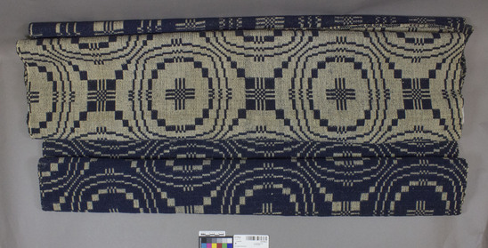 Hearst Museum object titled Coverlet, accession number 2-62166a,b, described as Coverlet. Materials:  wool. Techniques: Summer and Winter weave, Wheel of fortune pattern. Navy and white colors. Both pieces 97” x 40”. Coverlet is in two pieces, meant to be sewn together to make one. Woven by Polly Bacon for her marriage to Edward West Thomas, 1825 in Pike County, New York. Wool probably hand spun.