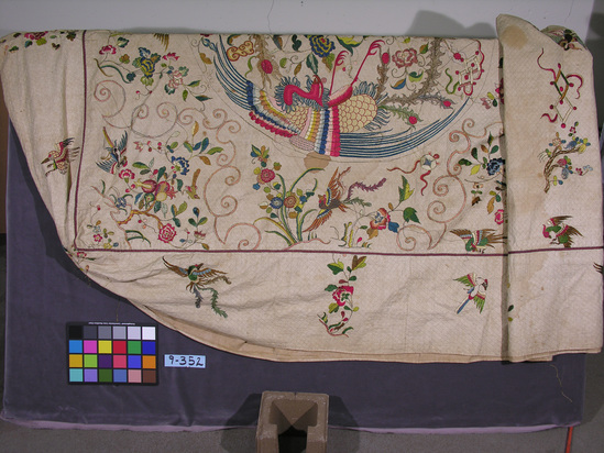 Hearst Museum object titled Bedspread, accession number 9-352, described as Bedspread; quilted, off-white cotton backed with linen; overall diamond stitched design; varicolored silk embroideries outlined in metal-wrapped threads; Chinese-style florals, birds, phoenixes, pomegranates, endless knot, etc.; damage to metal threads; width 2.18 cm, length 2.61 cm.